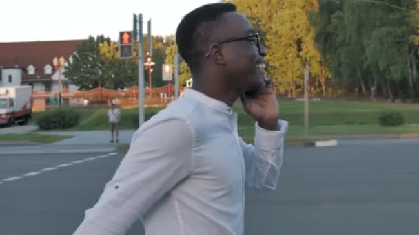 Closeup smiling happy black man talking mobile phone outdoors. Close up of cheerful african american businessman having phone call, business conversation while crossing a road — Stock Video