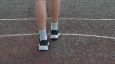 Kadın basketbolcunun ayaklarının spor ayakkabılarla tek başına basketbol oynadığı yakın plan.