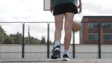 Kadın basketbolcu şehir parkında salya akıtıyor. Top zıplıyor, zıpla. Beyaz spor ayakkabılar, spor giysiler, bronzlaşmış deri. Genel görüş. Spor ve özgürlük kavramı.