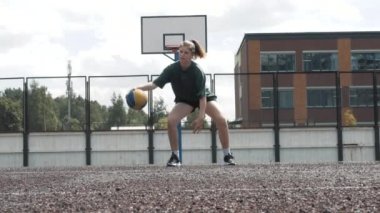 Genç bir kız basketbolcunun yerel sahada antrenman ve egzersiz yaptığı görüntüleri kapatın. Beyaz golf çoraplı genç bir kadın basketbol topuyla çapraz atlama eğitimi alıyor.