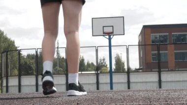 Profesyonel sahada şortlu ve beyaz çoraplı bayan basketbolcu topa vuruyor. El kamerasıyla çekilmiş. Açık havada.