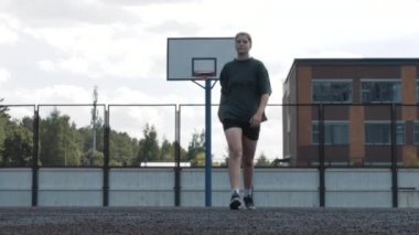 Terli, yorgun bayan basketbolcu yerel spor sahasında yürüyor ve sonra kameranın önünde oturuyor, yorgun genç kız dinleniyor.