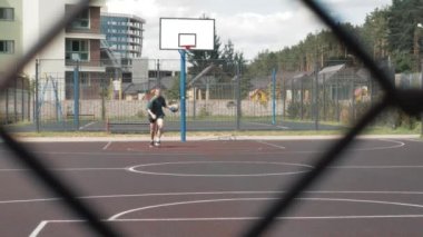 Güzel, genç, profesyonel bir bayan tek başına basketbol oynuyor, yerel sahada antrenman yapıyor, tek başına spor yapıyor, topla oynuyor.