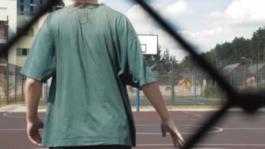 Genç uzun boylu bayan bir basketbolcunun arka plan görüntüleri yerel sahada antrenman ve egzersiz yapıyor. Beyaz golf çoraplı genç bir kadın basketbol topuyla çapraz atlama antrenmanı yapıyor.