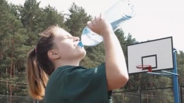 Plastik şişeden taze soğuk su içen terli bayan basketbolcu spor müsabakasında yorgun genç kız.