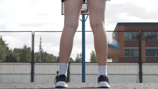 Vrouwelijke basketbalspeler dribbelt op de speelplaats. De bal is springt, stuitert. Witte sneakers en sportkleding, gebruinde huid. Algemeen zicht. Begrip sport en vrijheid. — Stockvideo