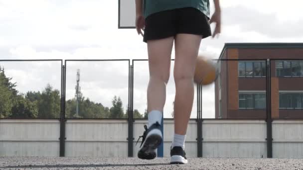 Vrouwelijke basketbalspeler dribbelt op de speelplaats. De bal is springt, stuitert. Witte sneakers en sportkleding, gebruinde huid. Algemeen zicht. Begrip sport en vrijheid. — Stockvideo