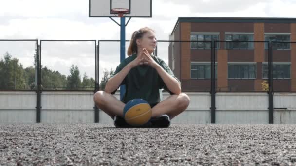 Thinking Happy female basketball player sitting with ball on court in open air, having rest, thinking about sport basketball competition strategy — Stock Video