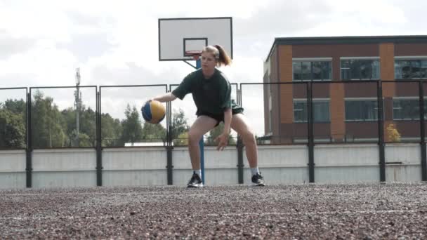 Közelíts meg egy felvételt egy fiatal kosárlabda játékosról, aki a szabadban edz és gyakorol a helyi pályán. Fiatal nő fehér golf zokni képzés kereszt pattogó kosárlabda — Stock videók