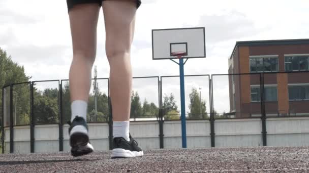 Jugadora de baloncesto femenina en pantalones cortos y calcetines blancos en cancha profesional corriendo con pelota y remolcando pelota a la red. Imágenes de mano. Al aire libre — Vídeos de Stock