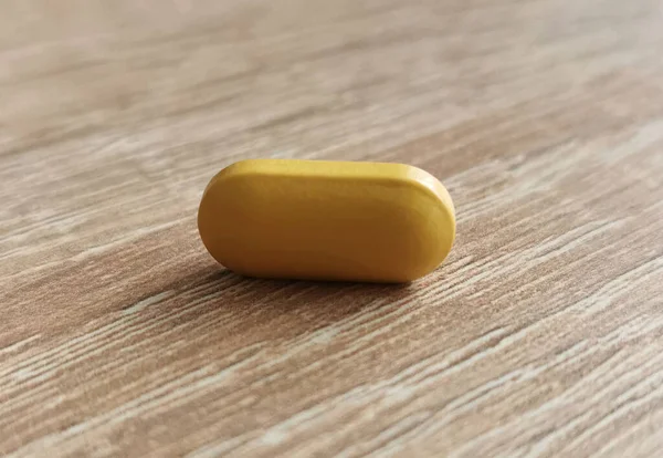 Single pill, dietary supplement on wooden table.