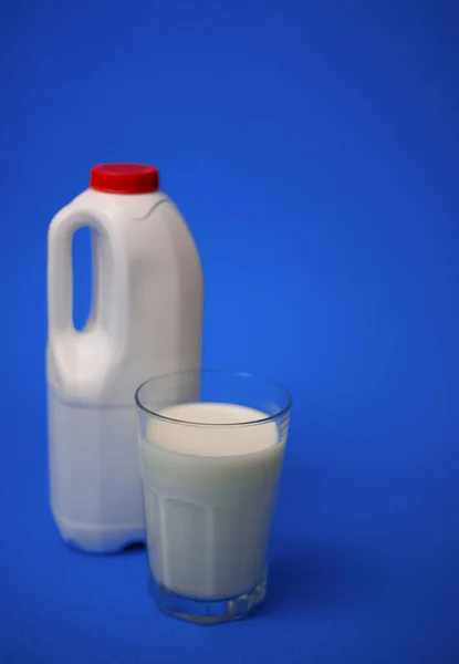 Airtight one gallon milk jug with a red cap and full glass milk on blue background