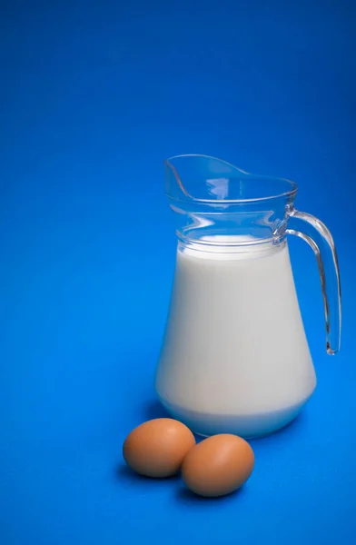 Leche Una Jarra Vidrio Dos Huevos Sobre Fondo Azul — Foto de Stock