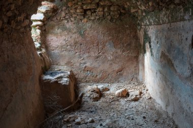 Eski terk edilmiş bir su tankının içinde, taştan yapılmış, yerde bazı taşlar ve kuru bir dal var.