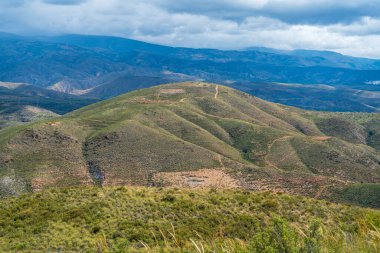Bitkilerle kaplı dağlık bir arazi, gökyüzü bulutlu.