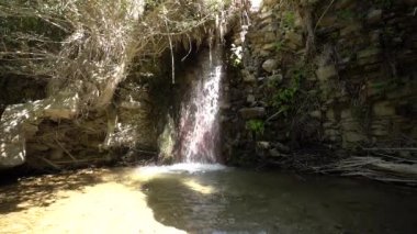 Güney İspanya 'da bir nehirde şelale var. Şelalenin yanında bitki örtüsü var. Metal örgülü taş bir duvar var.