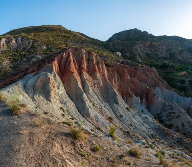 İspanya 'nın güneyindeki dağlık bölge, dağ bitki örtüsüyle kaplı, toprak birkaç renk tonu var, terk edilmiş bir çiftlik evi var ve gökyüzü mavi.