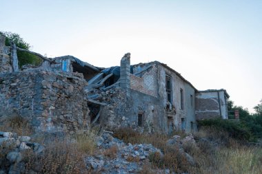 Eski bir çiftlik evinin kalıntıları, çiftlik evi taş ve tuğladan yapılmış, kuru bitki ve ağaçlar var.