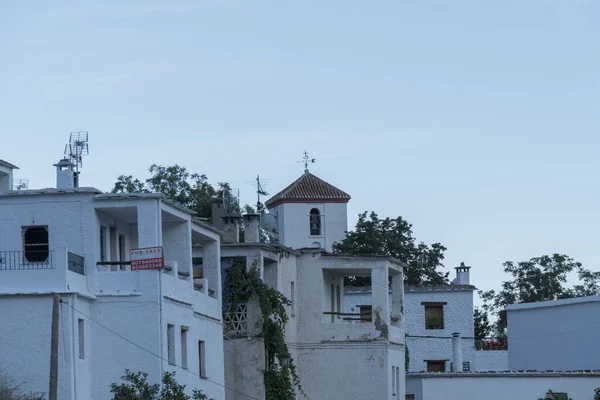 village with houses painted white, the houses have windows, balconies and terraces, there is a church tower, the sky is blue