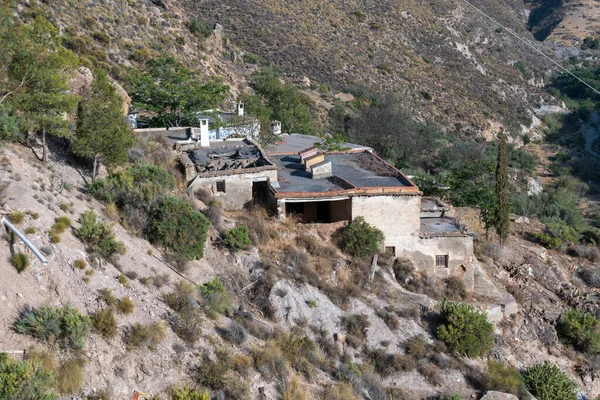 group of houses on the side of a mountain, there are trees around, on the slope there are bushes