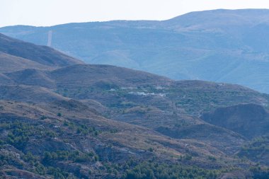 Dağın eteğindeki beyaz evlerden oluşan küçük bir kasaba. Kasabanın çevresinde bitki örtüsü var ve gökyüzü açık.