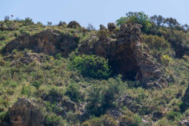 Güney İspanya 'nın dağlık arazisi, dağ bitki örtüsüyle kaplı ve büyük kayaları var, ağaçlar var ve gökyüzü açık.