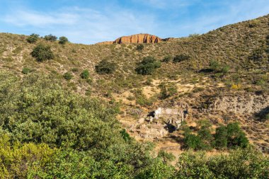İspanya 'nın güneyindeki dağlık arazide ağaçlar ve çalı bitkileri var. Eski bir çiftlik evinin kalıntıları var. Gökyüzünde çok az bulut var.