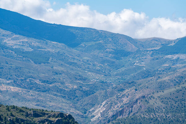 mountainous landscape in southern Spain, the mountain is covered with vegetation and there are clouds in the sky