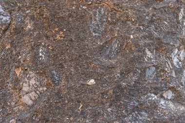 Koyu renk kaya arka planı ve dokusu büyük kayaya gömülü küçük taşlar var.