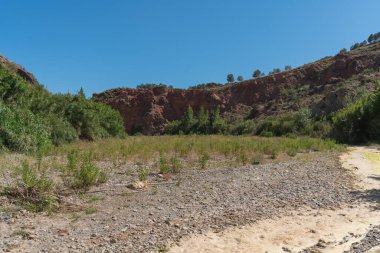 Güney İspanya 'nın dağlık arazisi. Sazlık ve ağaçların bol olduğu bir nehir var. Gökyüzü açık.