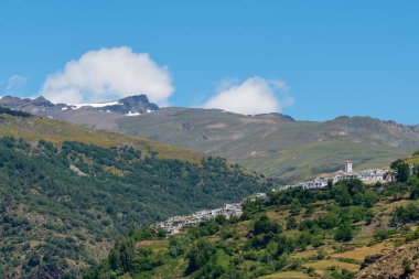 Sierra Nevada dağlarındaki Capileira kasabasında, dağlarda çam ormanları ve çalılar, dağlarda kar, gökyüzünde bulutlar var.