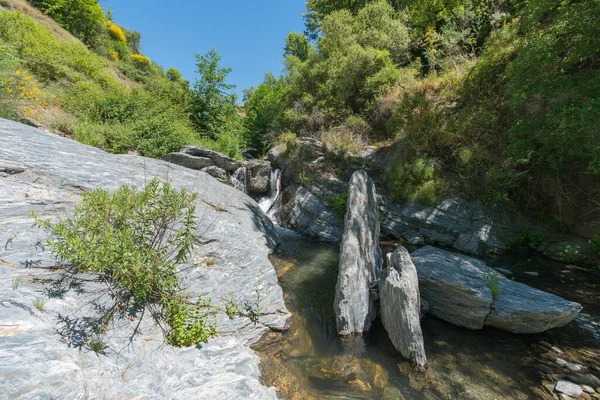 結晶性の川の植生に囲まれ ある川のベッドの石は 木々や茂みと山の領域ですが 空は明確です ストックフォト