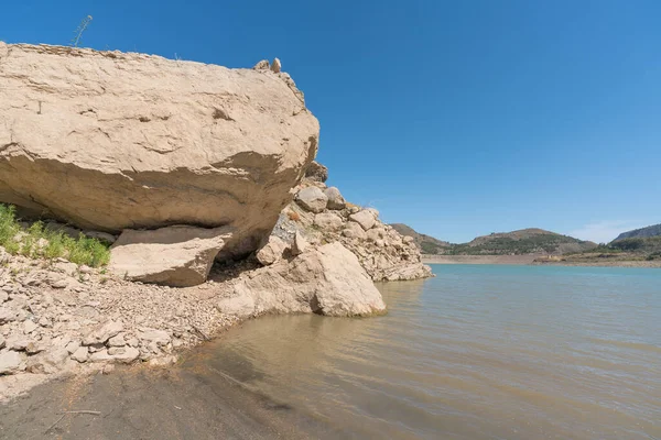 area of large rocks in the Beninar reservoir, there are stones, there is little grass between the rocks, the mountains have trees and bushes, the sky is clear