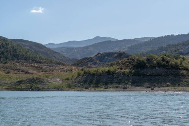 Beninar rezervuarındaki dağ manzarası, dağda ağaçlar ve çalılar var, gökyüzü açık.