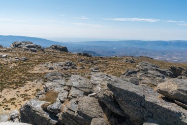 Calar Alto 'da dağın tepesinde kayalar, çalılar var, dağlık bir alan, gökyüzünde bulutlar var.