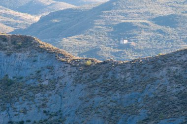 Granada vilayetinde bitki örtüsü olan dağlık bölgede çalılar ve ağaçlar var. Dağın yamacında terk edilmiş bir çiftlik evi var.