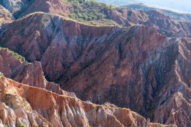 Arazi zamanla aşınmış, dağlık bir bölge, yeryüzünün farklı gölgeleri var, çalılar var ve gökyüzü aynalı.