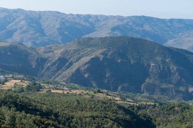 Güney İspanya 'da Sierra Nevada' da dağlık bir arazi, bir vadi var, bir holm meşesi ormanı var, birkaç ev var.