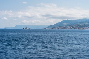 Messina şehri ve mavi gökyüzü arka plan ile açık denizde yelken bir feribot ile Messina Boğazı genel bakış. Yatay görünüm