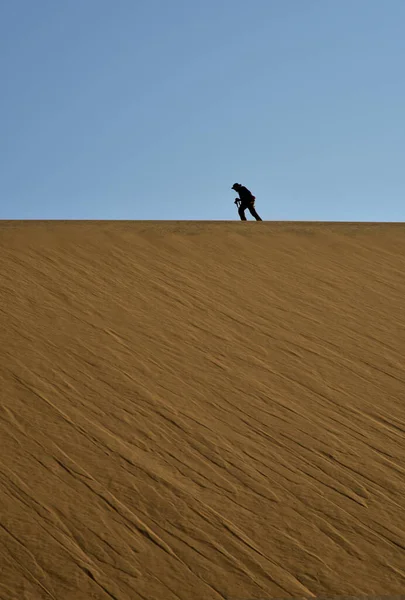A big flat Namib Desert dune surface with a windswept pattern and the silhouette of a photographer on it