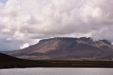 Tipik bir Karoo kumtaşı dağının tepesinde dramatik bulutlar ve ön planda bir baraj var.
