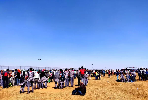 Okul öğrencilerinin bir hava gösterisini izlediği hevesli ve heyecanlı bir kalabalık.