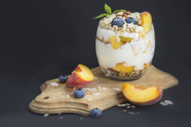 Sağlıklı yaban mersini, şeftali ve cevizli parfe koyu arkaplanda bir bardakta