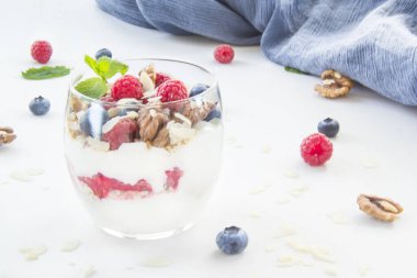 Sağlıklı yaban mersini, ahududu ve beyaz arka planda bir bardakta ceviz parfe.