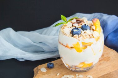 Sağlıklı yaban mersini, şeftali ve cevizli parfe koyu arkaplanda bir bardakta