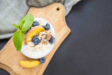 Sağlıklı yaban mersini, şeftali ve cevizli parfe koyu arkaplanda bir bardakta