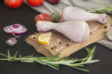 Biberiyeli çiğ tavuk budu, domates ve siyah ahşap arka planda baharatlar. Yaratıcı atmosfer dekorasyonu.