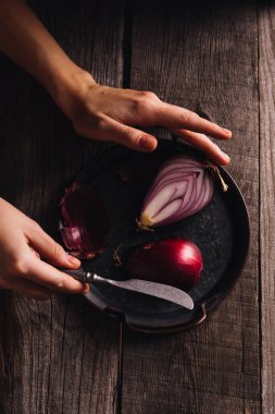 Kadın ahşap bir masada soğan kesiyor.