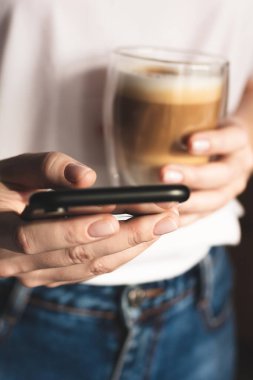 Elinde akıllı telefon ve bir fincan kahve tutan kadın.