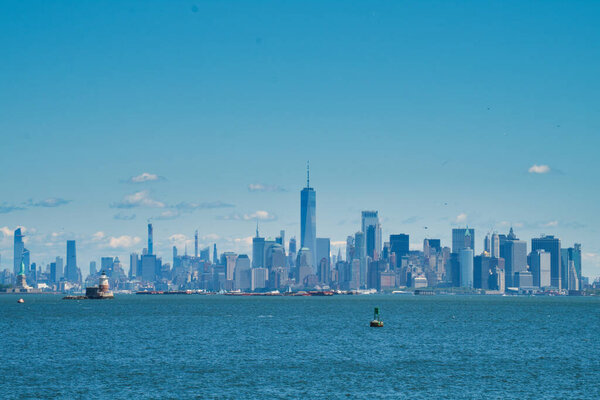 Statue of Liberty and lighthouse in front of Manhattan on a sunny summer day